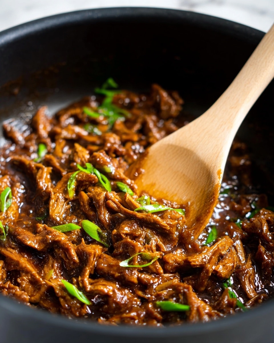 The image shows a close-up of a dark pan filled with shredded pieces of brown meat covered in a shiny, thick sauce. Scattered throughout the meat are small, bright green slices of spring onions, adding a fresh color contrast. A light wooden spoon is stirring the meat from the right side, its smooth texture clearly visible. The sauce glistens under the light, making the meat look moist and flavorful. The background has a white marbled texture. photo taken with an iphone --ar 4:5 --v 7