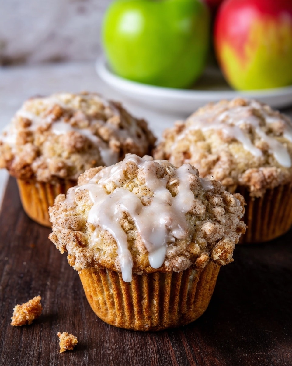 The image shows a group of cinnamon sugar-coated muffins arranged on a white marbled surface. There are eight muffins in total, with one broken open in the center revealing a moist, golden brown inside full of small crumbs and a slightly rough texture. The muffins have a light brown sugar crust on top, giving them a grainy look. On the left side, a small white bowl contains more cinnamon sugar, visible as a fine, light brown powder. In the lower right corner, a partially sliced red apple with a bright green leaf adds a splash of color to the scene. The light is warm and natural, creating soft shadows. Photo taken with an iphone --ar 4:5 --v 7