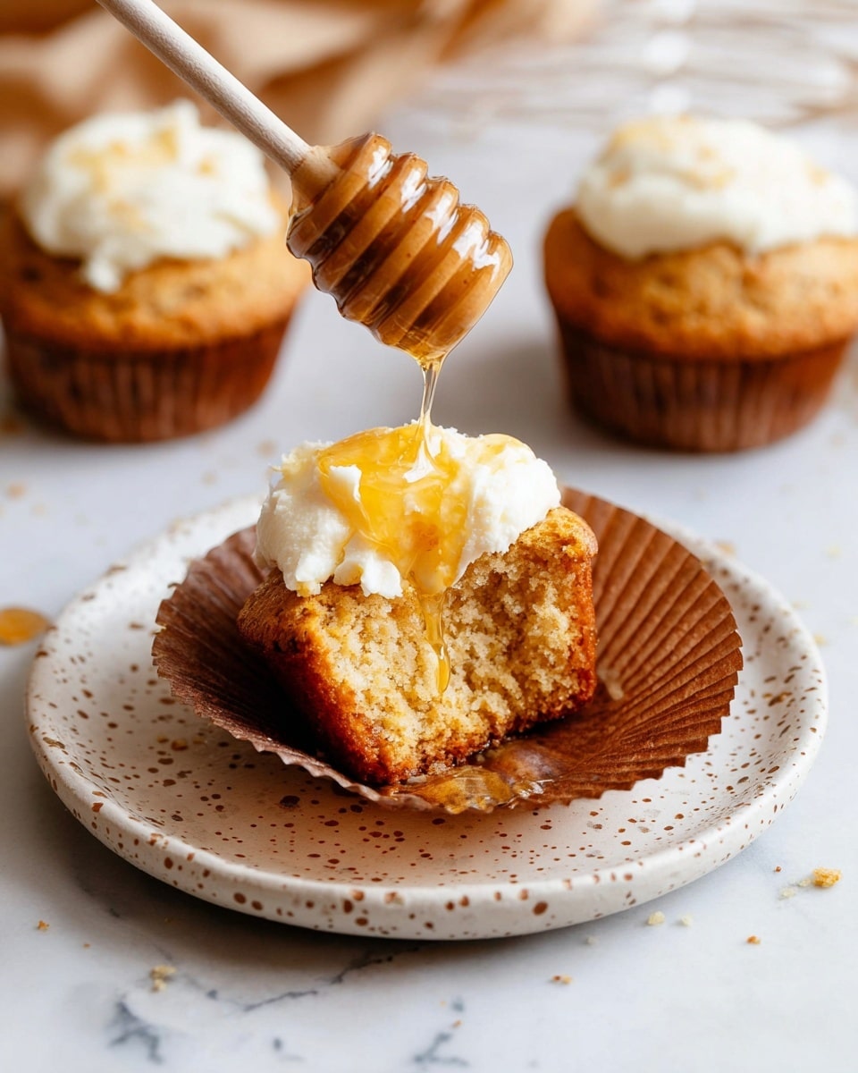 Several golden brown muffins are displayed on a white marbled surface, with some inside light brown paper liners and others fully exposed. One muffin is opened in half, showing a soft, moist interior with a crumbly texture. A small white bowl filled with swirled creamy butter or spread with a light golden drizzle sits nearby, while a clear glass jar of honey with a wooden honey dipper rests to the side. The scene is well lit with natural light, highlighting the warm tones of the muffins and the smooth surface of the butter and honey jar. photo taken with an iphone --ar 4:5 --v 7