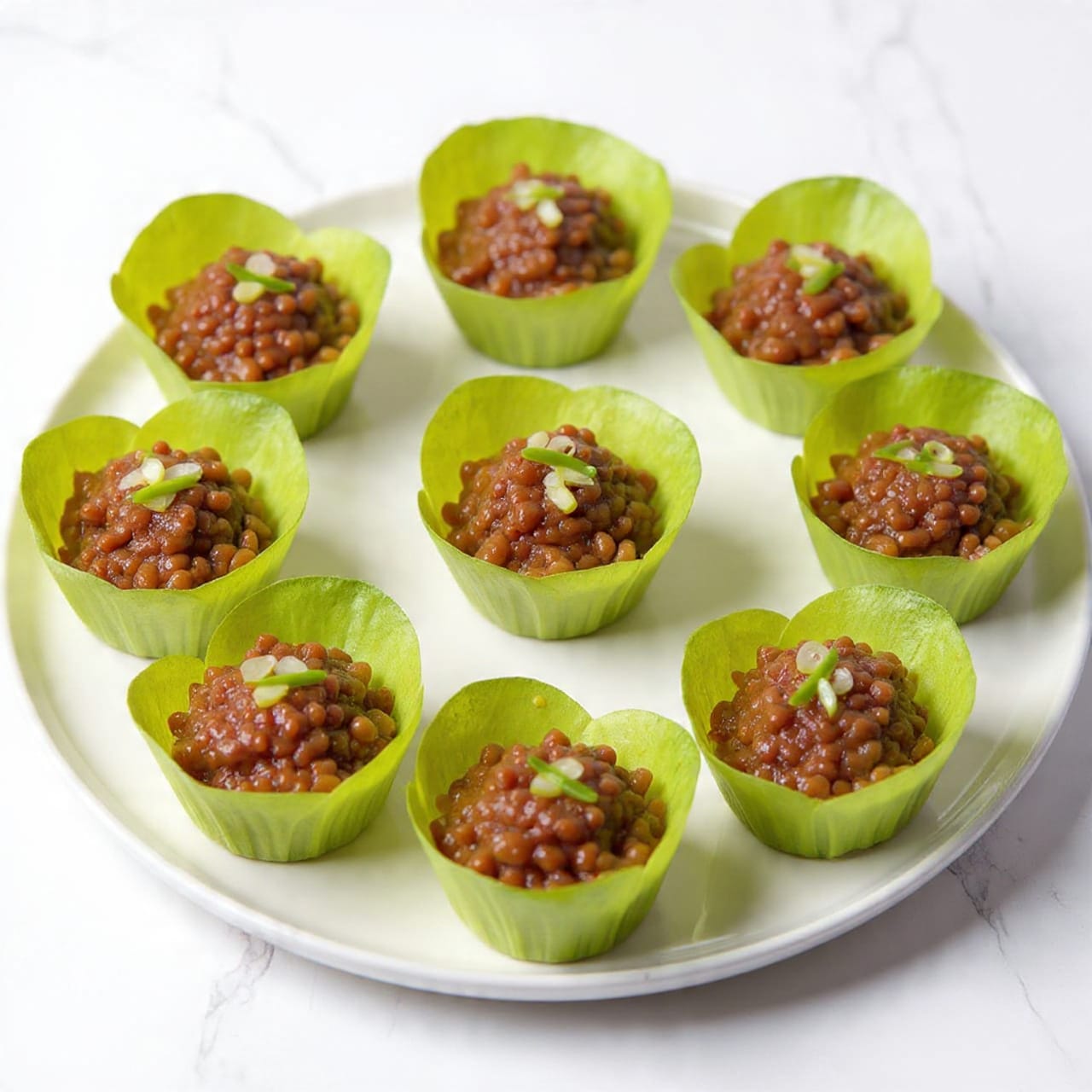 The dish shows seven green lettuce cups placed evenly on a round white plate on a white marbled surface. Each lettuce cup forms a bowl shaped with fresh, crisp, light green leaves, with the outer leaves being a darker green. Inside each cup, there is a dark brown cooked minced meat filling that has a slightly glossy texture. The meat filling is topped with thinly sliced green spring onions scattered over each cup, adding a fresh touch. The overall look is neat, fresh, and colorful with a contrast between the green lettuce and the rich brown meat filling. photo taken with an iphone --ar 4:5 --v 7