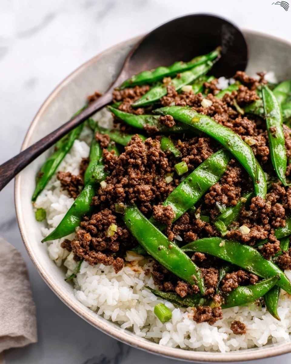 The image shows a white bowl filled with a base layer of plain white rice, topped with cooked ground meat that is dark brown and crumbly in texture. Bright green fresh snap peas or green beans are scattered evenly over the meat, adding a fresh pop of color. Small bits of chopped garlic or onions are sprinkled across the top. The bowl is placed on a white marbled surface, with a dark spoon resting on the side, and a woman's hand gently holding the bowl. photo taken with an iphone --ar 4:5 --v 7
