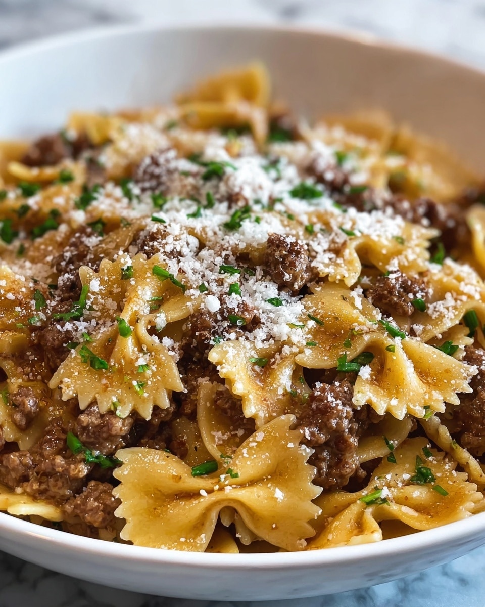 A close-up view of a white bowl filled with farfalle pasta mixed with browned ground meat pieces. The pasta is a golden yellow color and is coated lightly with a brown sauce. On top, there is a layer of white grated cheese sprinkled evenly, adding a powdery texture. Small chopped green herbs are scattered over the cheese, creating little bright green spots. The background is a white marbled surface. Photo taken with an iphone --ar 4:5 --v 7