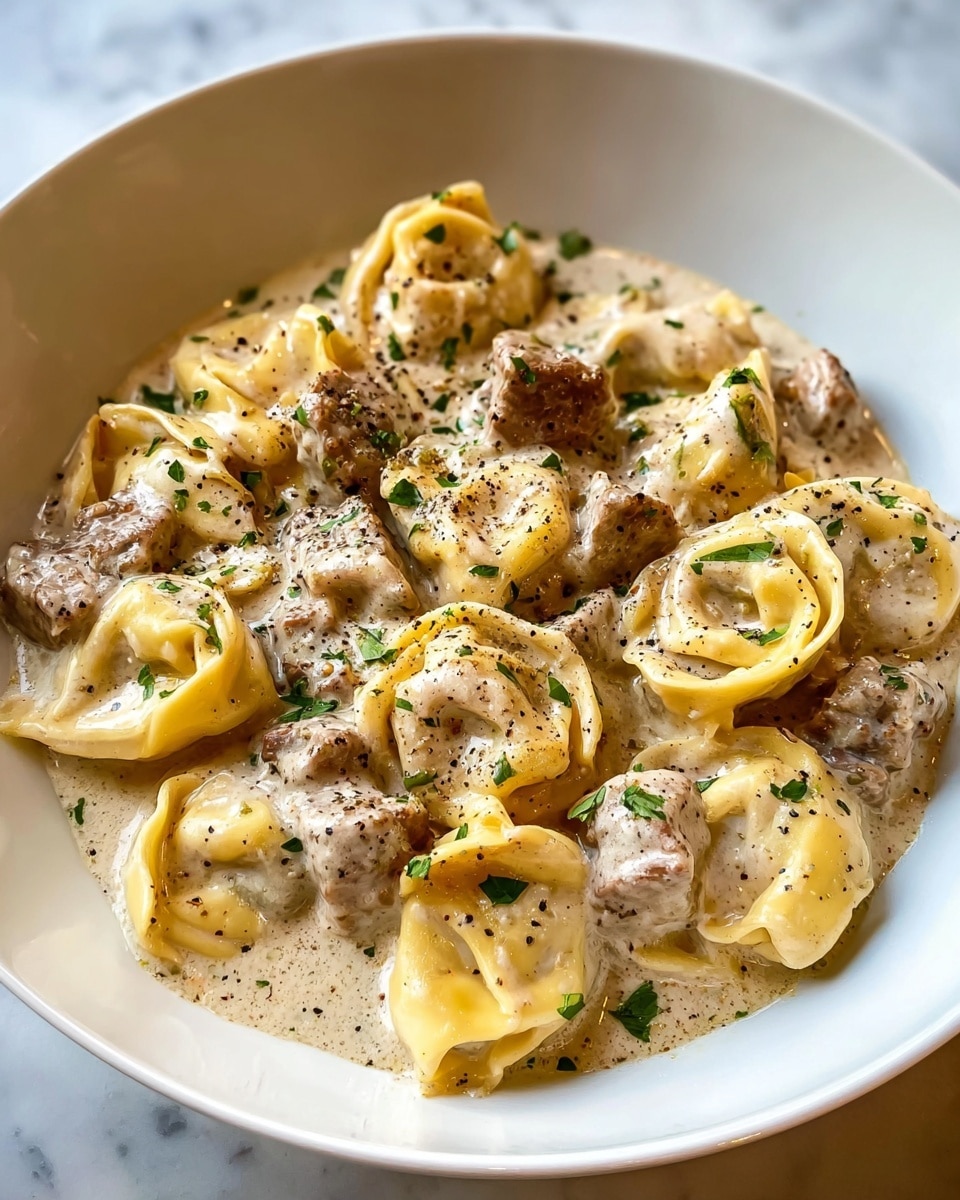 A white bowl holds about ten pieces of pale yellow tortellini pasta filled with meat, all covered in a creamy, light beige sauce. Among the pasta are chunks of tender brown meat scattered evenly. The creamy sauce is smooth and thick, coating every piece. Small green parsley bits are sprinkled on top along with a dusting of black pepper, adding color contrast. The white bowl sits on a white marbled surface. photo taken with an iphone --ar 4:5 --v 7
