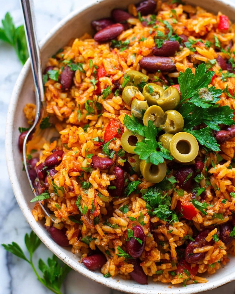A close-up of a white bowl filled with a colorful rice dish made of orange rice mixed with red kidney beans, small red tomato pieces, and green herbs scattered throughout. On top, green olive slices and fresh green parsley leaves add a fresh touch. A spoon sticks into the right side of the bowl. The bowl sits on a white marbled surface. photo taken with an iphone --ar 4:5 --v 7