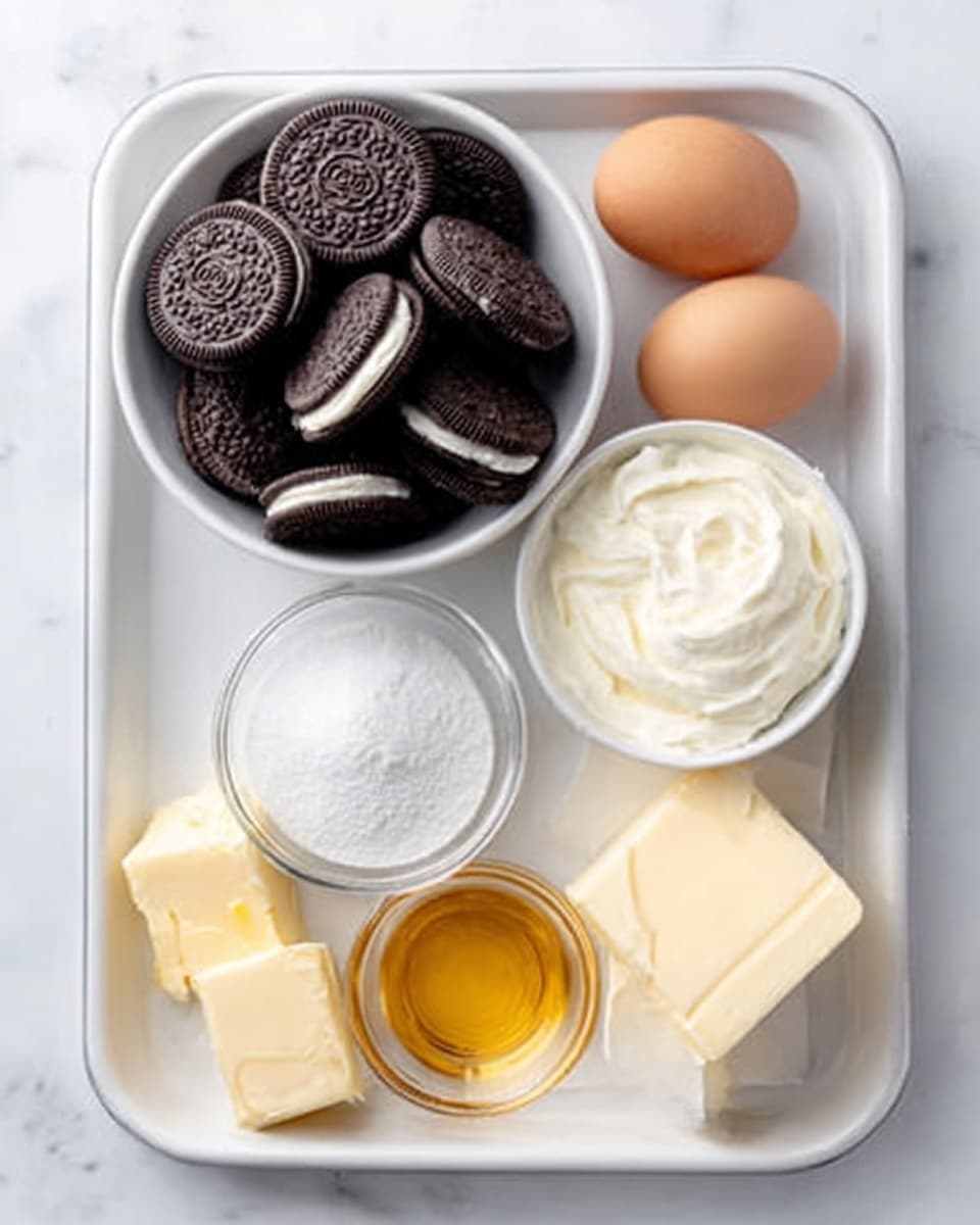 A white tray on a white marbled surface holds several ingredients arranged neatly: a white bowl filled with dark chocolate sandwich cookies stacked together, two brown eggs placed side by side near the top right, a small white bowl of creamy white frosting beside the eggs, a clear glass bowl filled with fine white sugar near the bottom left, a small portion of yellow butter and a block of white cream cheese close to the bottom right, and a small amount of golden honey or syrup in front. Photo taken with an iphone --ar 4:5 --v 7