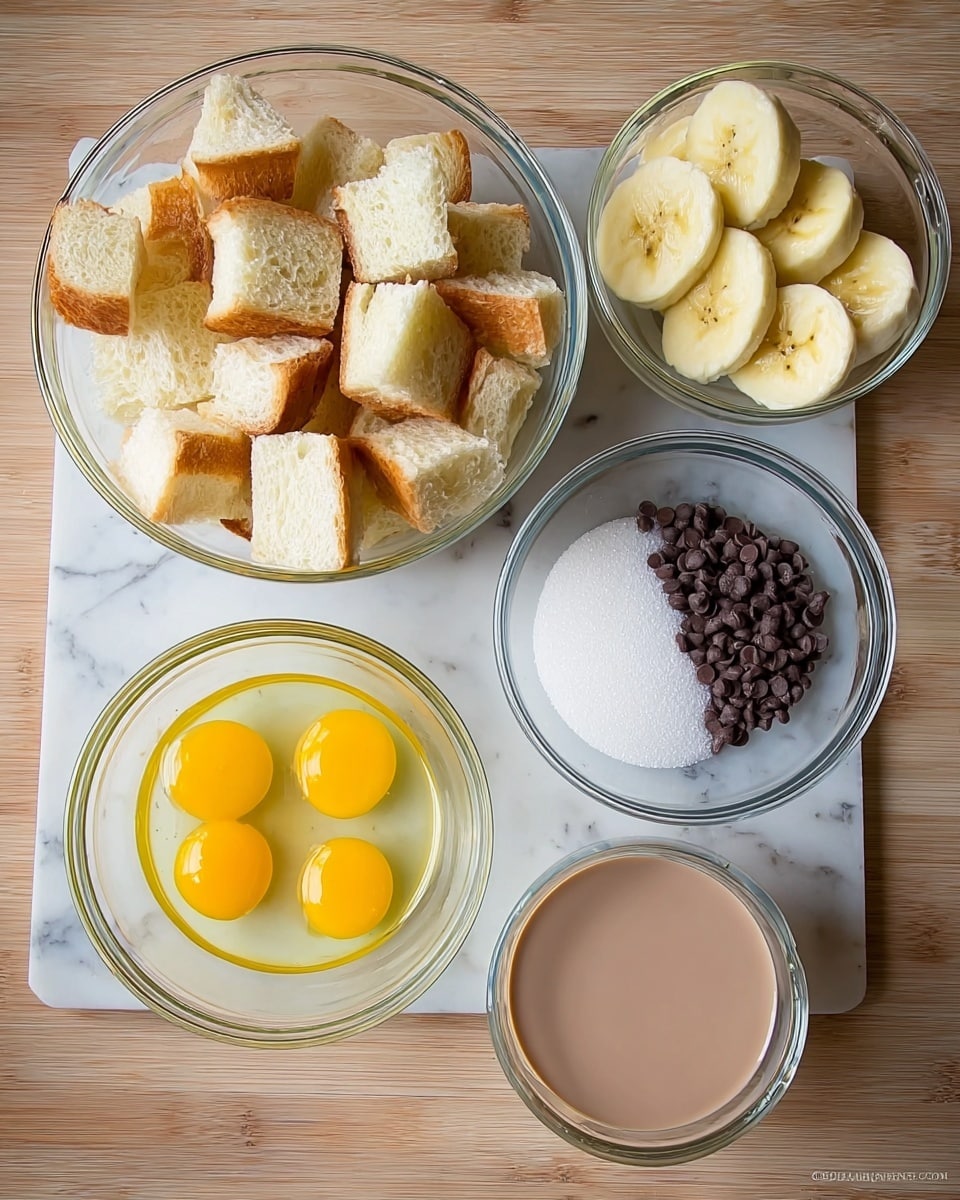 The image shows five clear glass bowls arranged on a white marbled surface. The largest bowl in the top left is filled with many pieces of white bread with golden brown crusts, cut into cubes. To the right of it is a smaller bowl that holds three slices of yellow banana arranged in a line on top of a pile of small dark chocolate chips. Below this bowl is a medium bowl with three raw yellow egg yolks surrounded by clear egg whites. In the center is a small bowl filled with white granulated sugar. To the left of the sugar bowl is another medium bowl filled with a smooth light brown liquid, likely chocolate milk. The bowls are placed on a white marbled surface with a woman’s hand not visible in the frame. Photo taken with an iphone --ar 4:5 --v 7