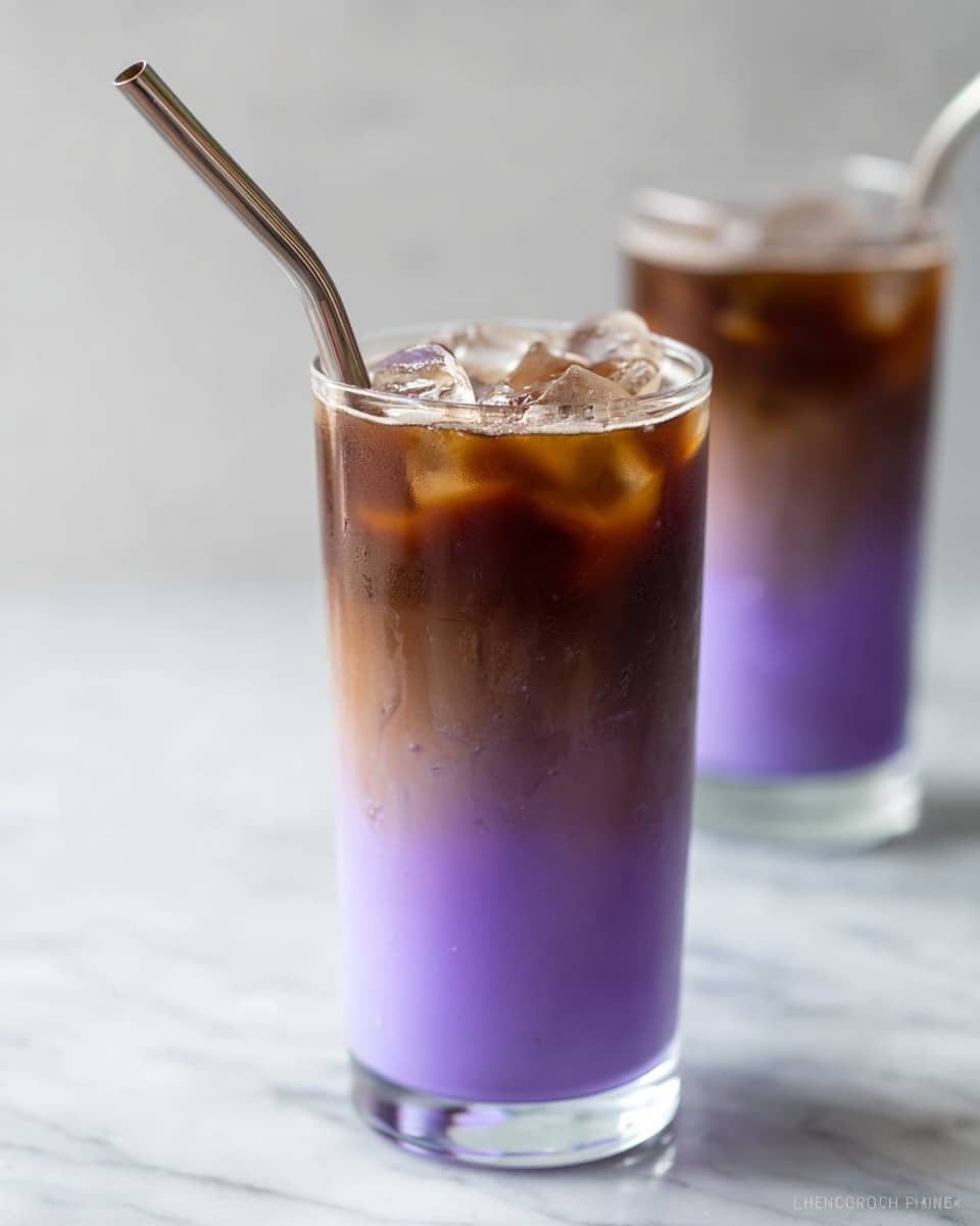 Two tall clear glasses of a two-layer iced drink sit on a white marbled surface. The bottom layer is a bright purple, smooth and creamy, filling about two-thirds of the glass. The top layer is a dark brown liquid with ice cubes floating on top, creating a clear separation between the purple and brown layers. One glass is in the foreground with a metal straw sticking out, and the other glass is slightly blurred in the background. The photo is bright and clean, taken with an iphone --ar 4:5 --v 7