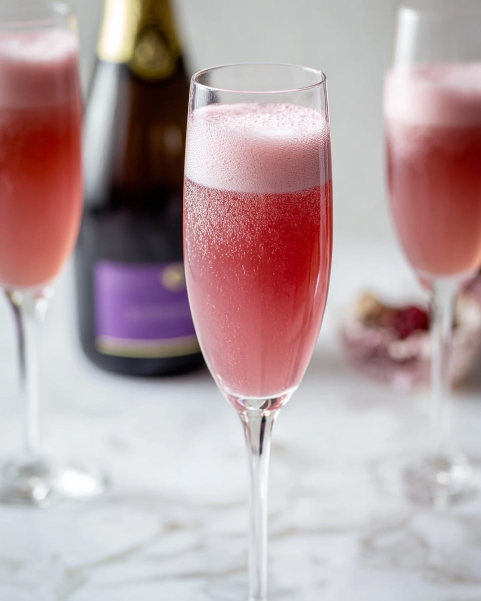 The image shows a tall, clear champagne glass filled with a pink sparkling drink that has a layer of light pink foam on top with tiny bubbles rising through the liquid. In the background, there are two other glasses also filled with the same pink drink, slightly out of focus, and a dark bottle with a purple label. All items are set on a white marbled surface. photo taken with an iphone --ar 4:5 --v 7