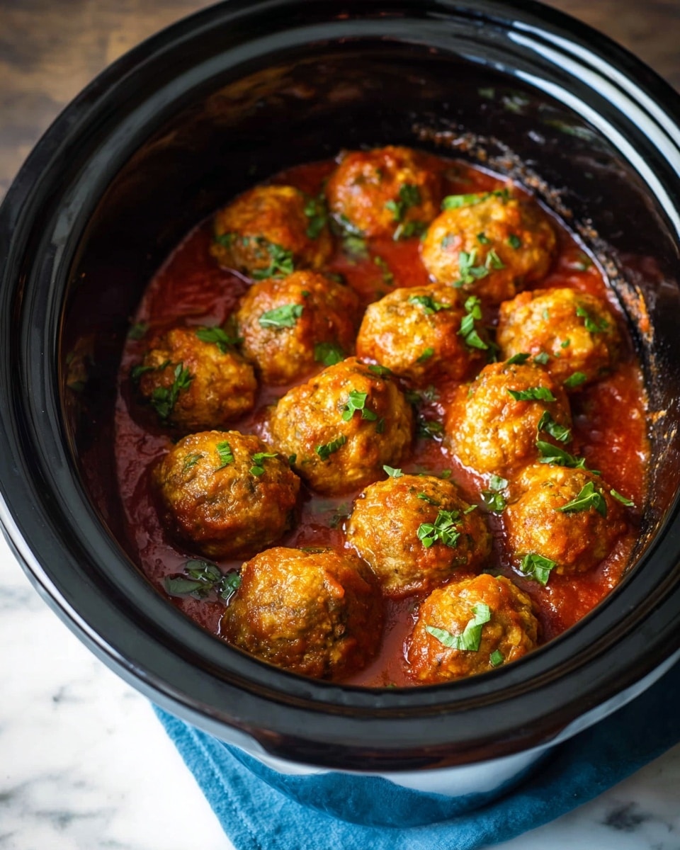 A black crockpot filled with about ten golden-brown meatballs that have a slightly rough texture, each topped with bits of bright green chopped basil. The meatballs sit in a thick, red tomato sauce pooled at the bottom, with some sauce lightly coating the sides and the meatballs. The crockpot is shiny with some reflections, and it's placed on a white marbled surface with a hint of a blue cloth around the base. photo taken with an iphone --ar 4:5 --v 7