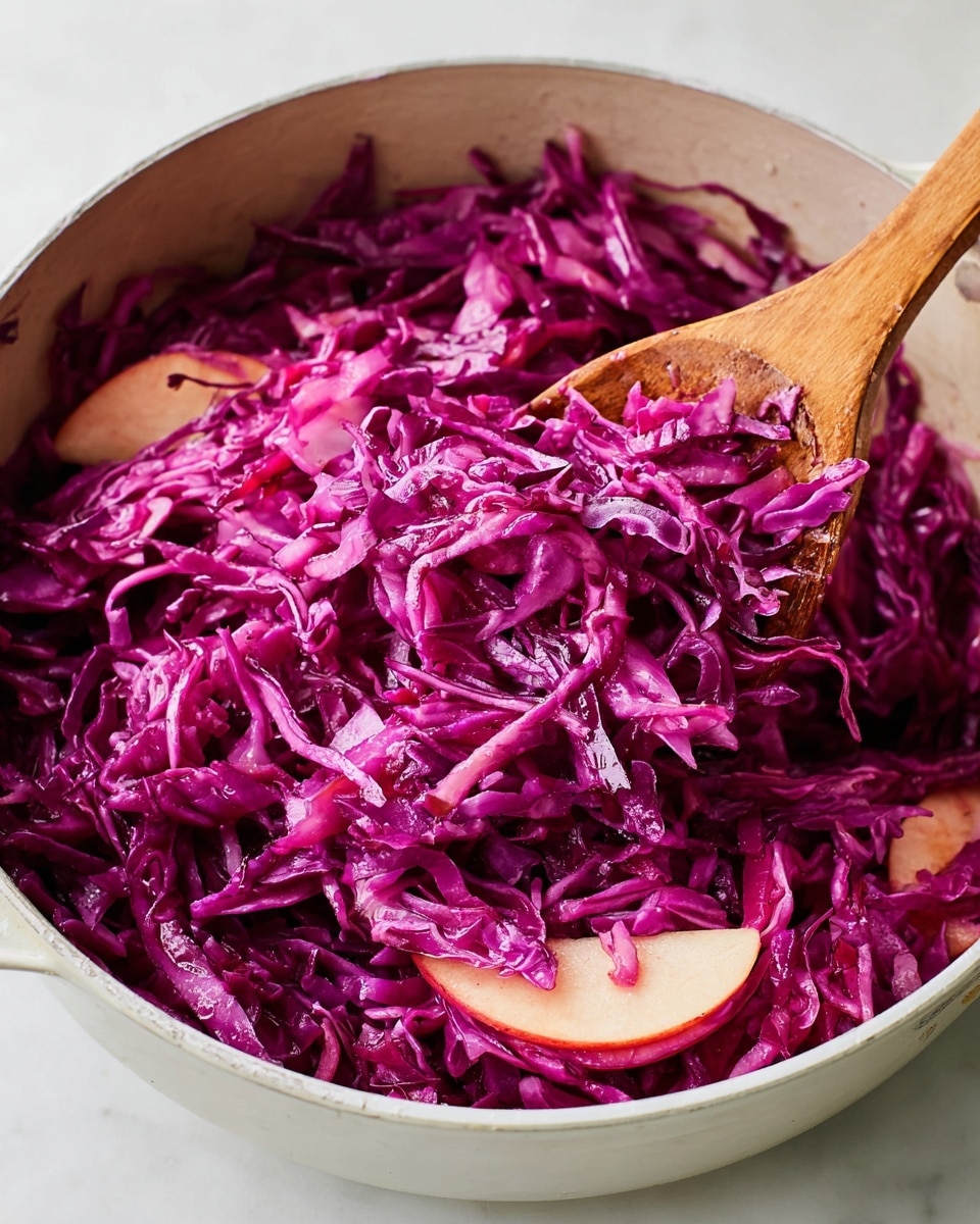 A close-up of a white bowl filled with shredded bright purple cabbage mixed with thin slices of pink and pale apple. Inside the bowl, there is a wooden spoon partially lifting a pile of the shredded cabbage, showing the soft and slightly shiny texture. The mixture has a fresh and juicy look, with the bowl resting on a white marbled surface. Photo taken with an iphone --ar 4:5 --v 7