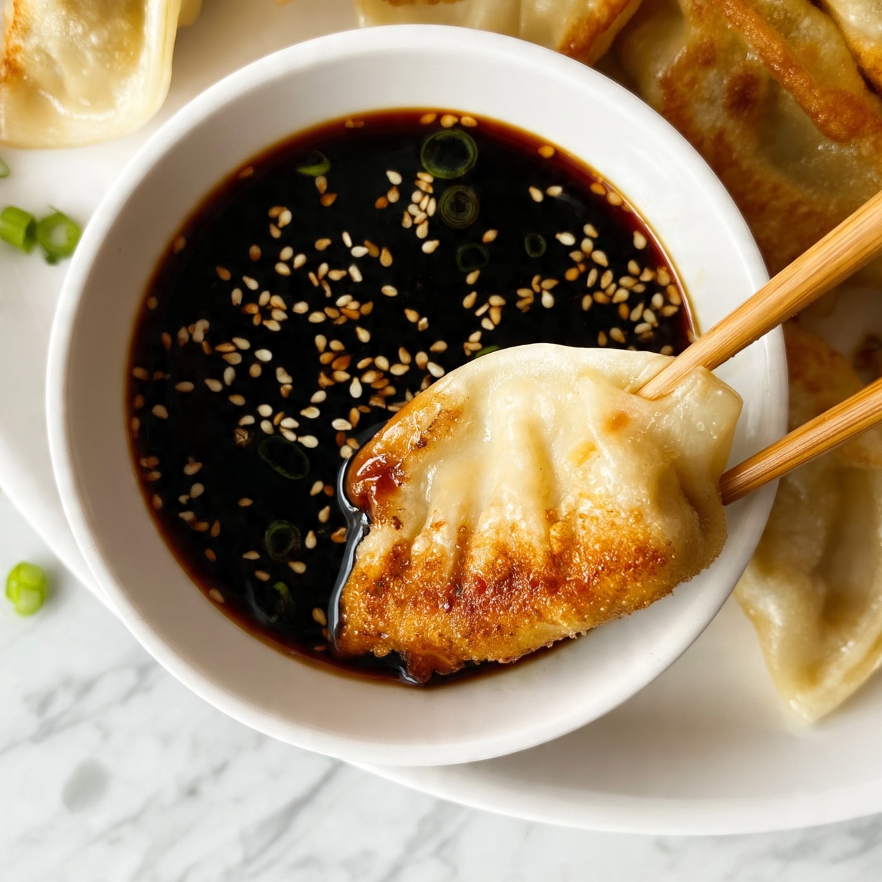 A close-up of a white bowl filled with dark soy sauce topped with light brown sesame seeds and small green onion rings, with a single golden-brown fried dumpling partially dipped into the sauce and held by light brown chopsticks, showing the dumpling's light beige, crispy, and slightly blistered texture on the bottom half, surrounded by more dumplings on a white plate on a white marbled surface, with a few green onion pieces scattered near the bowl, photo taken with an iphone --ar 4:5 --v 7